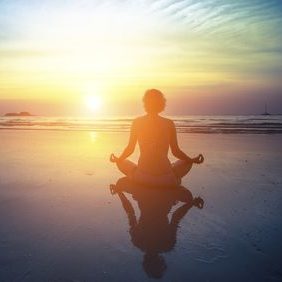 Young woman silhouette practicing yoga on the beach at amazing sunset