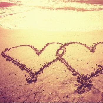 Vintage style photo of two hearts shape draw on the sand of a beach in morning time