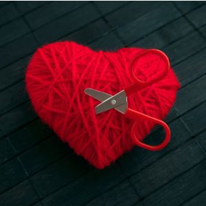 Red thread heart with red stuck scissors on black wooden background. 