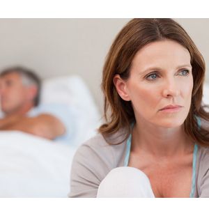 Sad mature woman on bed with her husband in the background