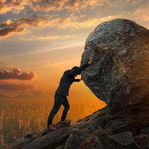 man pushing large stone up to hill 