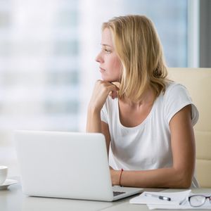 Young attractive woman at a modern office desk, working with laptop, looking at the window