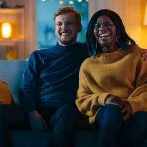 Happy Diverse Young Couple Watching Comedy on TV while Sitting on a Couch, they Laugh and Enjoy Show
