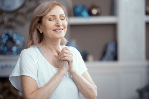 Happy mature Woman Is Pressing Her Arms To The Chest. Satisfied Woman With Closed Eyes Smiles And Presses Hands To The Chest