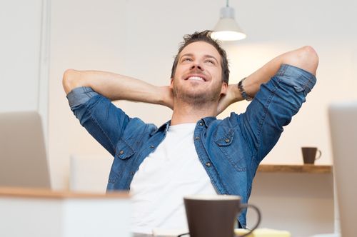 Happy young man sitting with hands behind head in office