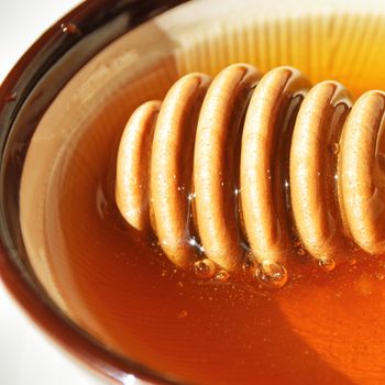 close up of honey and honey dipper in a bowl on a white background.