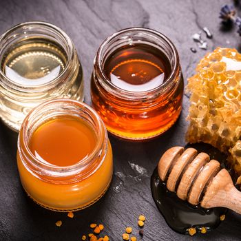 Honey in jar with honey dipper on black stone background