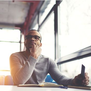 Pensive african american handsome man dressed in trendy outfit and glasses sitting in cafe