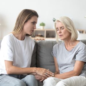 Loving adult daughter talking to sad old mother holding hand comforting upset older woman having problem