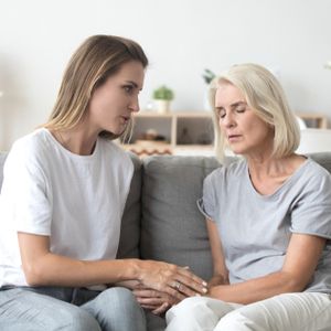 Loving adult daughter talking to sad old mother holding hand comforting upset older woman having problem