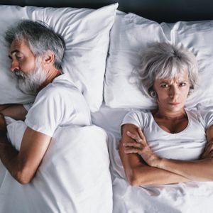 Overhead of senior couple in the bed. Pretty aged woman is angy with her sleeping husband.