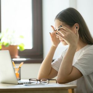 Tired ill female office worker massaging eyes, relieving stress from long hours working and looking at laptop screen