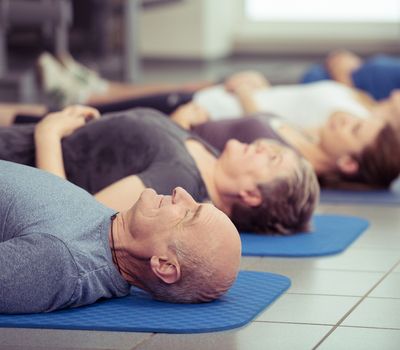 Senior couple participating in aerobics class at the gym with diverse people lying in a receding row on mats