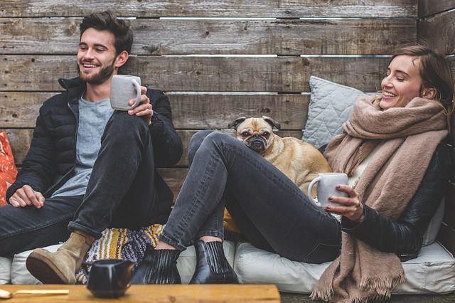 A young couple drinking from mugs and relaxing in a cabin, with a pet dog.