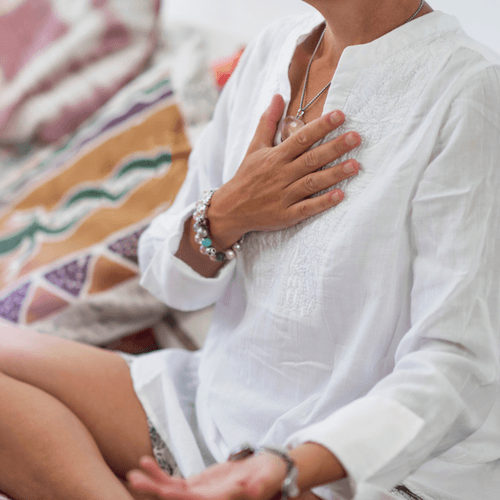 Self-Healing Heart Chakra Meditation. Woman sitting in a lotus position with right hand on heart chakra and left palm open in a receiving gesture.