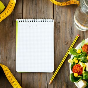 Workout and fitness dieting copy space diary. Healthy lifestyle concept. Salad, apple, dumbbell, water and measuring tape on rustic wooden table.