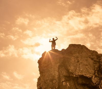 Man on top the edge of a cliff flexing his arms in victory.