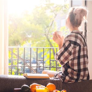 Young pretty woman sitting at opened window drinking coffee and looking outside enjoys of rest