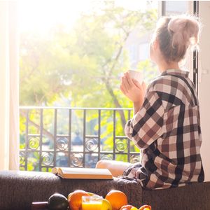 Young pretty woman sitting at opened window drinking coffee and looking outside enjoys of rest